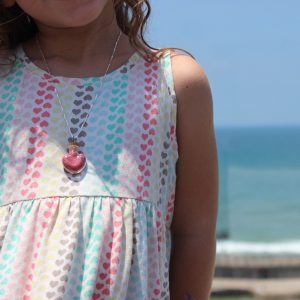 ילדה עם שמלת לבבות, עונדת שרשרת כסופה עם בקבוקון בצורת לב, ממולא בנצנצים