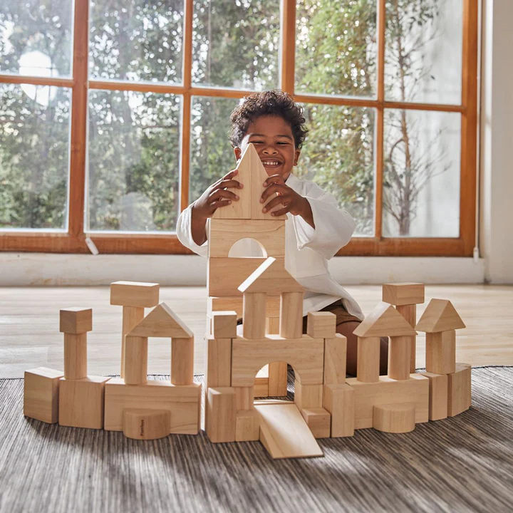 ילד משחק עם הבלוקים ומחייך, ומאחוריו חלון גדול עם עצים.