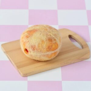 סופגנייה מלובדת מונחת על קרש חיתוך מעץ, שמונח על רקע של משבצות בצבעי ורוד ולבן