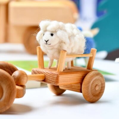 כבשה לבנה מלבד עומדת על צעצוע טרקטור מעץ